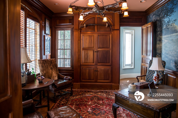 Dark stained wood stained home office with warm rust desert color with wood furniture, desk, lamp and oriental rug