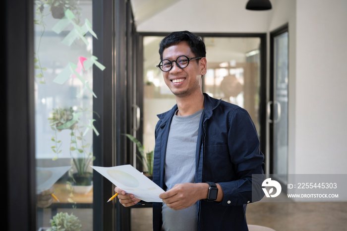 Young creative man standing in modern office and smiling to camera.