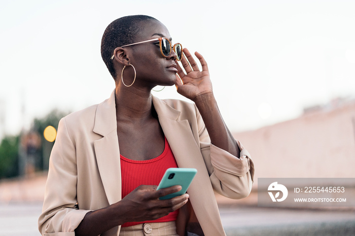 Elegant young woman wearing a fashionable beige trousers and jacket set holding phone