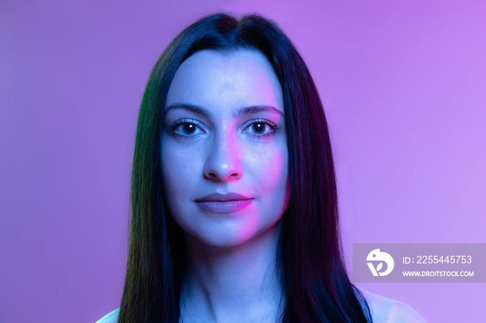 Portrait of adorable girl, young woman with long glossy dark hair isolated on purple background in neon light. Concept of beauty, art, fashion, emotions