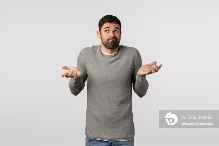 Funny bearded male in grey sweater, shrugging with hands raised sideways, smirk and look away as if dont know, cant help, standing indecisive, hiding truth, unwilling say, posing white background