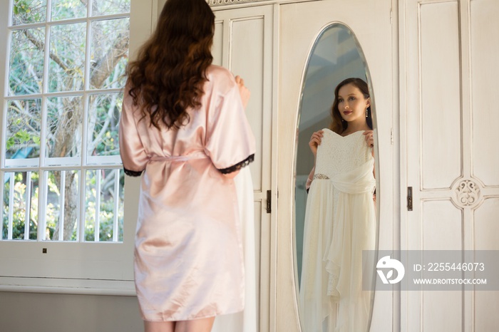 Bride trying on dress while standing by mirror at home