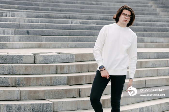 Man wearing white sweatshirt or hoodie and glasses outside on the city streets. Sweatshirt or hoodie for mock up, logo designs or design prints with free space