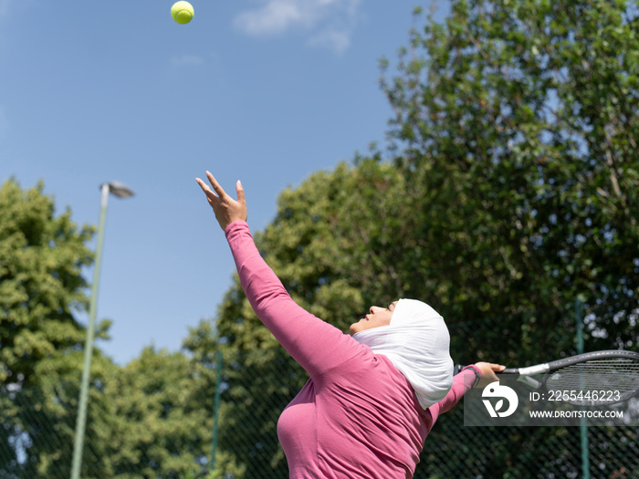 UK,Sutton,Woman in headscarf playing tennis in park