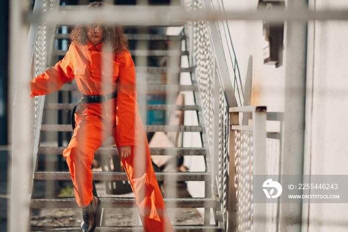 Young brunette curly woman in orange suit. Female in colorful overalls portrait