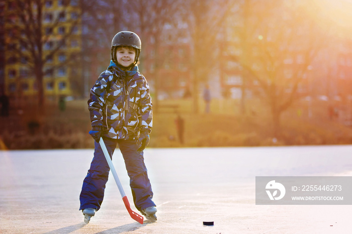 Children, playing hockey and skating in the park on frozen lake, wintertime on sunset