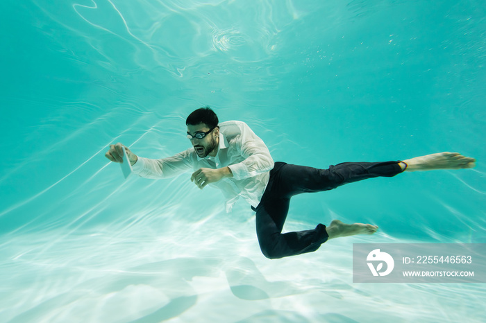 Muslim businessman in goggles holding mobile phone underwater in pool