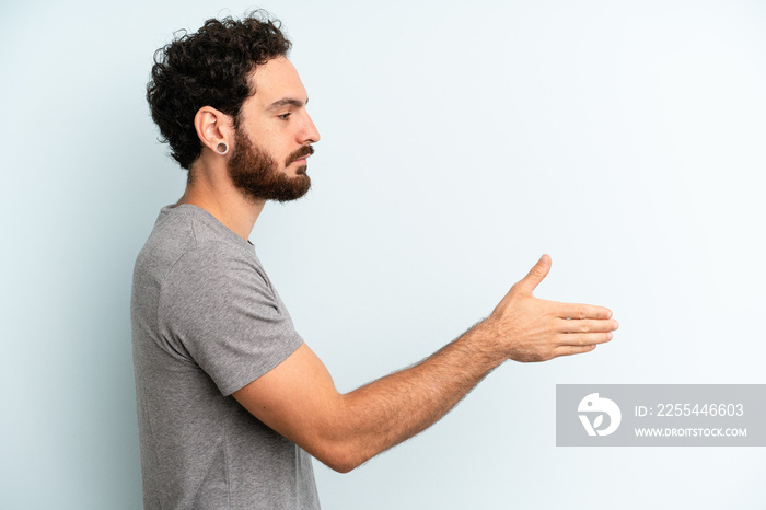 young adult bearded man smiling, greeting you and offering a hand shake to close a successful deal, cooperation concept