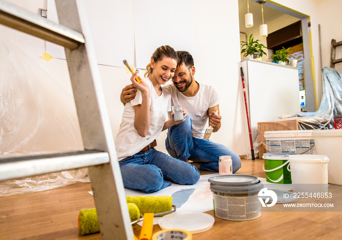 Young couple sitting on the floor choosing color for painting the wall in their home.