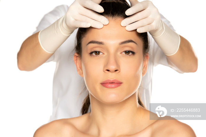 doctor’s hands in gloves checks a face of young woman on white background