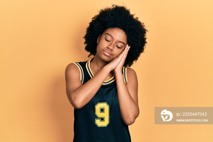 Young african american woman wearing basketball uniform sleeping tired dreaming and posing with hands together while smiling with closed eyes.