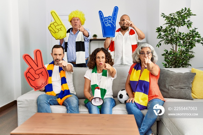 Group of senior people supporting soccer team at home pointing with finger to the camera and to you, confident gesture looking serious