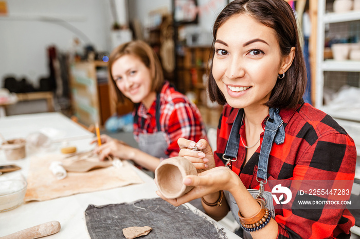 Young woman friends create clay and ceramic art dishes in pottery workshop