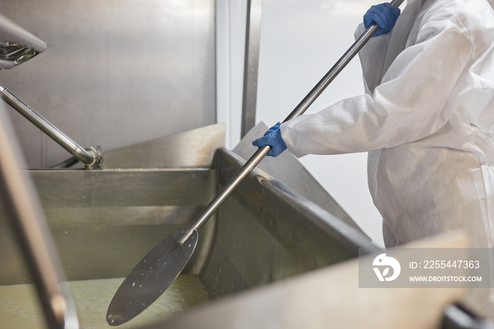 Cropped shot of unrecognizable worker mixing product at cheese and dairy factory, copy space