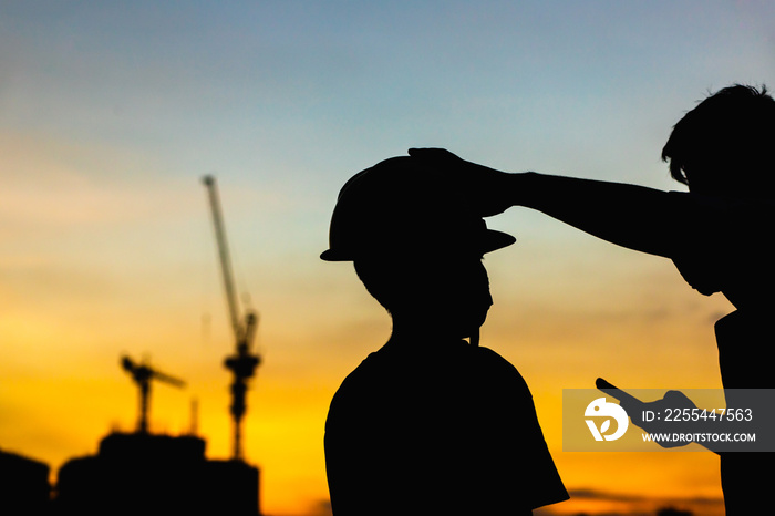 The silhouette of the happy father and son wearing a construction helmet holding hands expressing the joy of the sunset