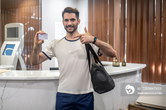 Bearded male standing at recepion desk, holding club card, pointing at it