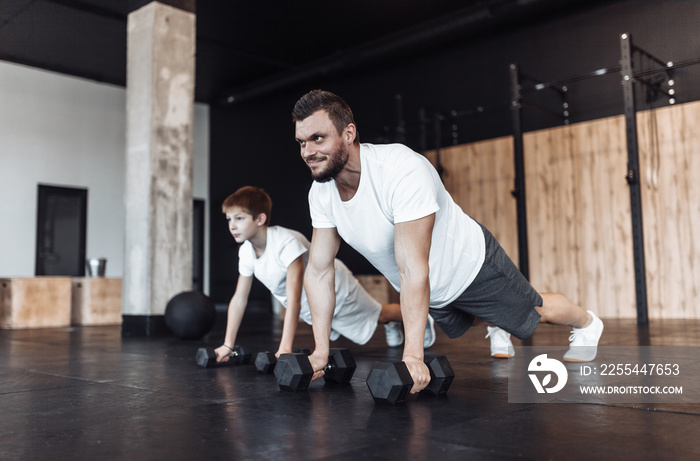 Healthy family concept. Father trainer and teenager son push ups with dumbbells in gym. Fitness, sports, active lifestyle