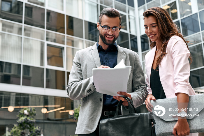 Preparation for meeting. Two young business people standing outside on the city street reading documents smiling cheerful