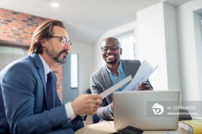 Dark-skinned businessman smiling while cooperating with colleague