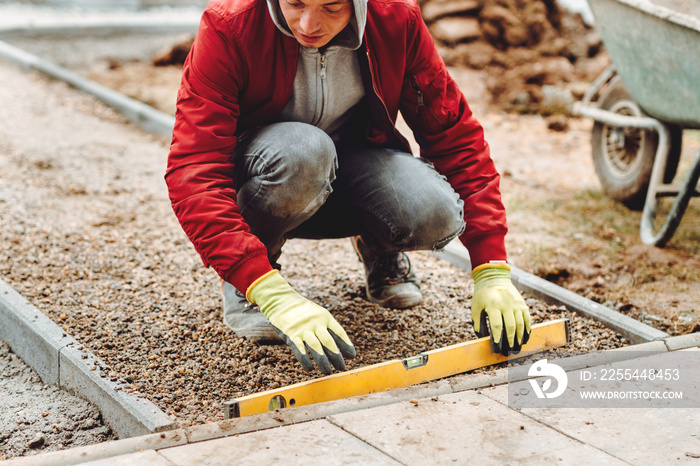 Close up of construction worker installing and laying pavement stones on terrace, road or sidewalk. Worker using pavement slabs and level to build stone sidewalk