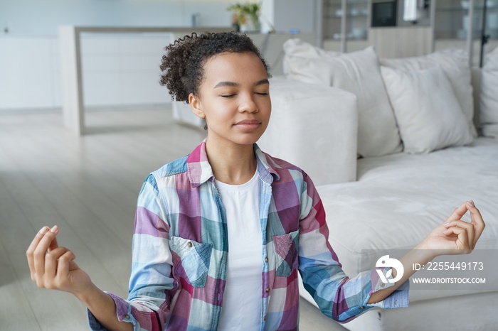 Calm mixed race girl meditates to relieve stress, does breathing exercise with mudra gesture at home