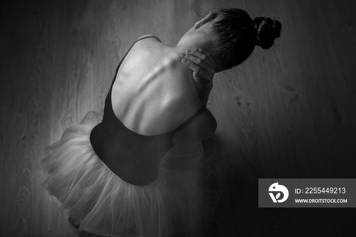 Tight back exhausting workouts and pain. Ballet dancer sits on the floor in dark lighted room stretches neck. Top view photo. Horizontal. Copy space