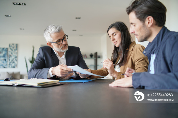 Attractive couple signing contract with real-estate agent in contemporary house