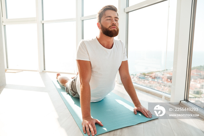 Bearded man doing yoga exercise over window background