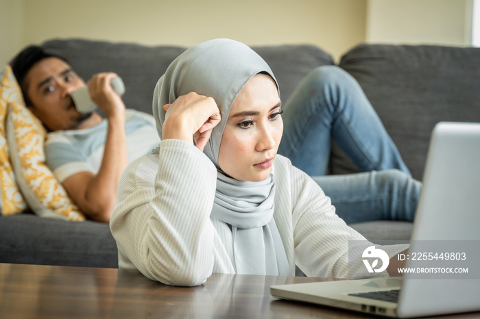 Stress looking wife work with her laptop and husband at the sofa