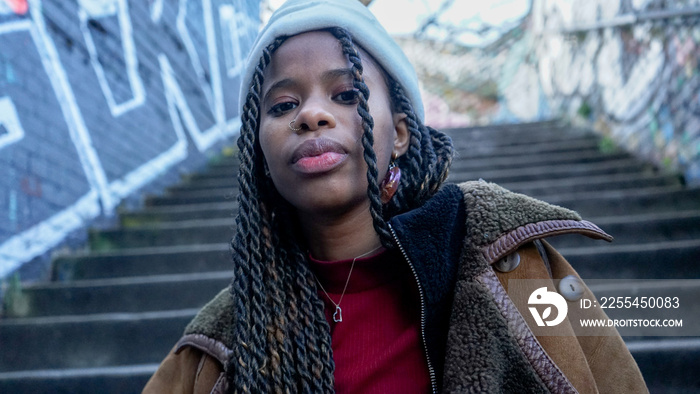 Portrait of young woman with braided hair and cap on steps outdoors