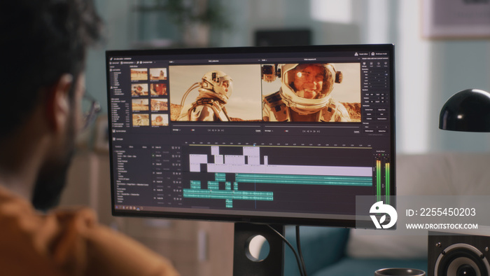 Back view of male content creator using computer to edit cosmonaut video during remote work from home