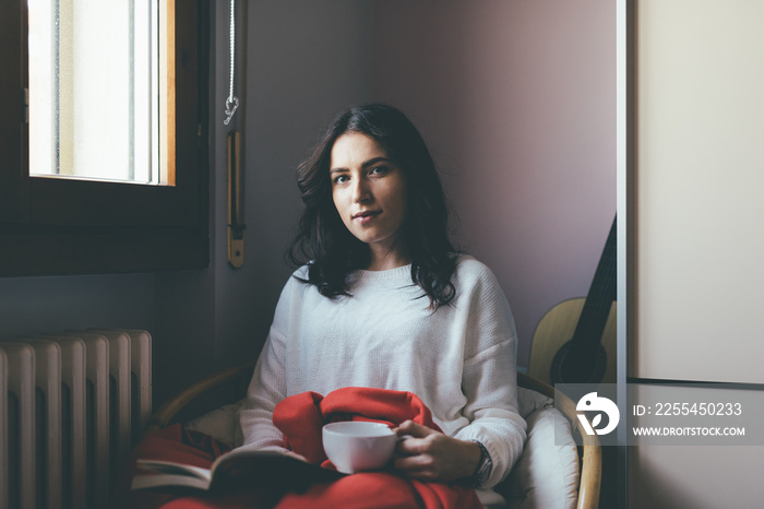 Portrait of young woman holding tea cup sitting on chair at home