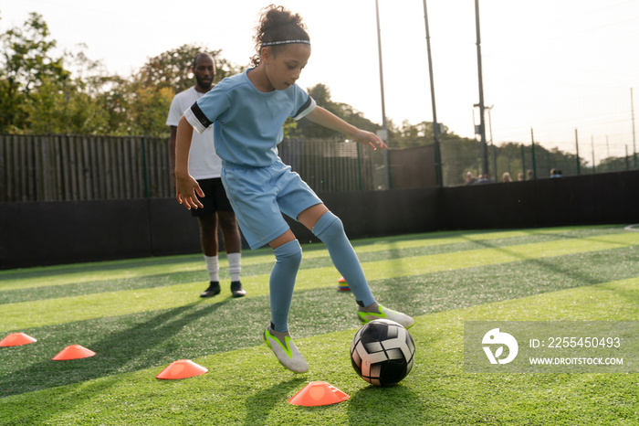 Coach watching girl (6-7) practicing on soccer field