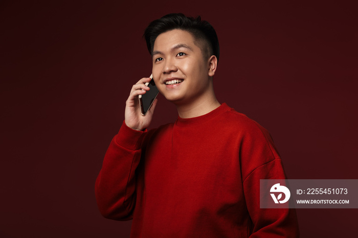 Image of joyful young asian man smiling and talking on mobile phone