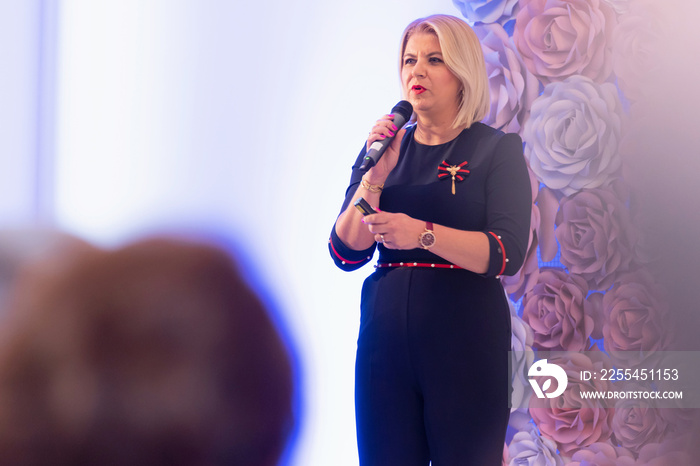 Beautiful business blonde woman with microphone in her hand speaking at the conference or seminar.