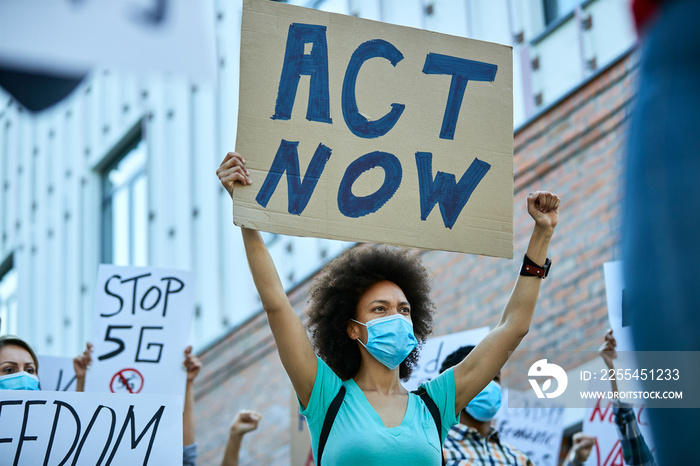 Below view of black woman with face mask protesting with crowd of people during coronavirus pandemic.