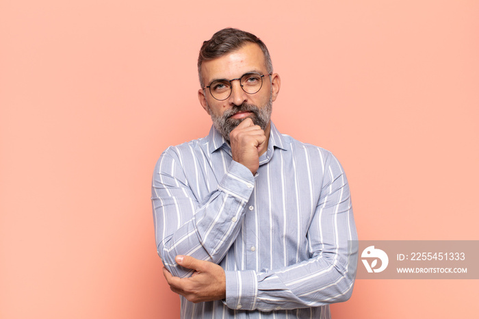 adult handsome man looking happy and smiling with hand on chin, wondering or asking a question, comparing options