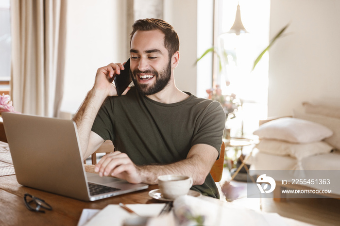 Photo of handsome mature man using laptop and smartphone while working in flat