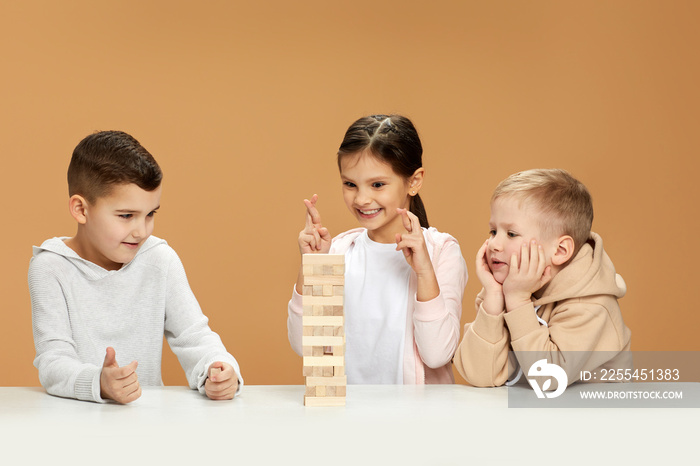 children plays with wooden constructor on desk.