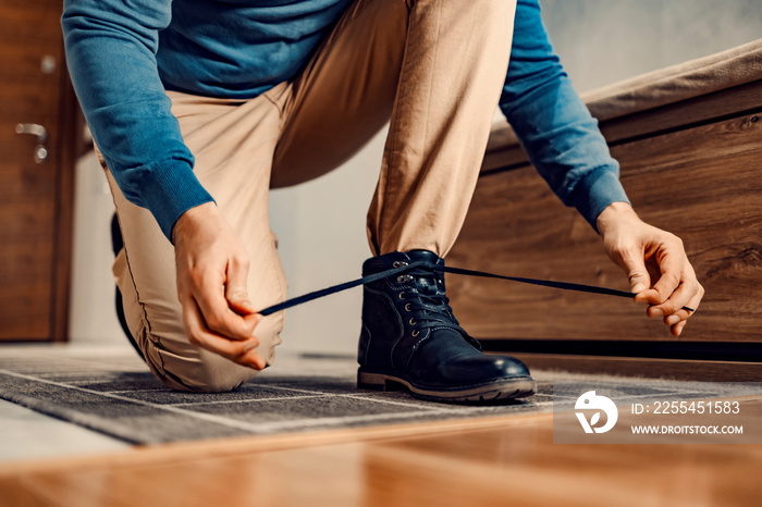 A man kneeling and tying shoelace on leather shoes and preparing to go out.