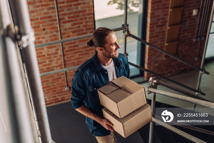 selective focus of smiling businessman holding boxes and walking on stairs in new office