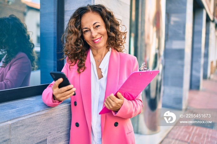 Middle age hispanic businesswoman smiling happy using smartphone at the city.