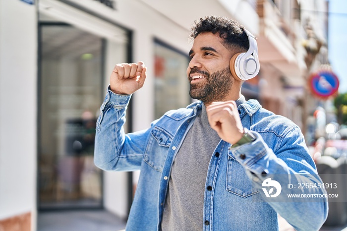 Young hispanic man listening to music and dancing at street