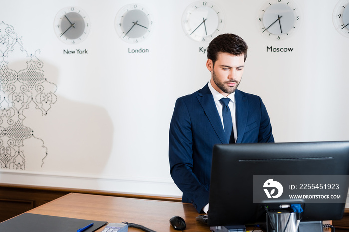 handsome receptionist in suit looking at computer monitor in hotel