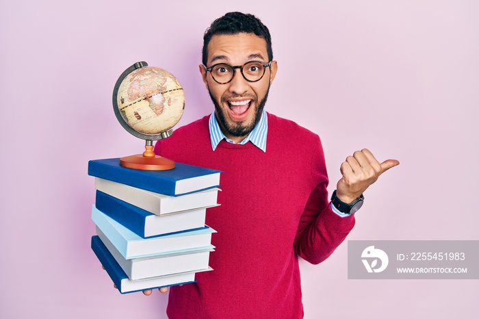 Hispanic man with beard geography teacher pointing thumb up to the side smiling happy with open mouth