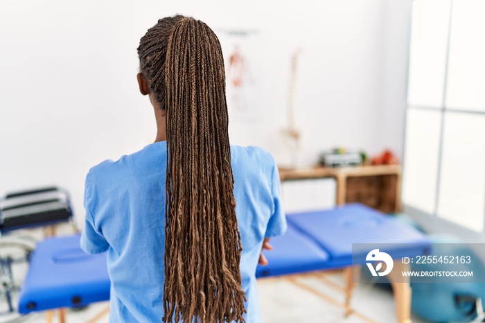 Black woman with braids working at pain recovery clinic standing backwards looking away with crossed arms