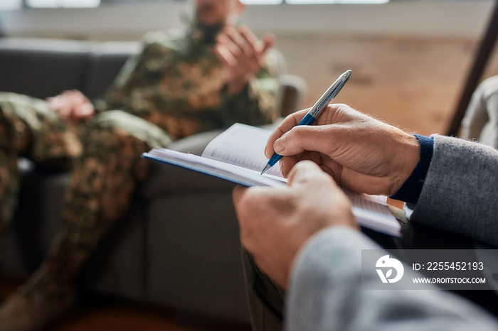 Notes. Close up of hands of psychologist making notes while communicating with military man during therapy session. Soldier suffering from depression, psychological trauma. PTSD concept