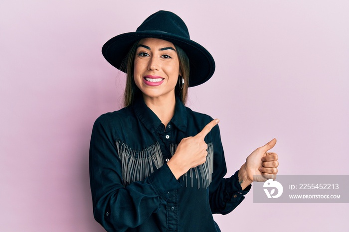 Young hispanic woman wearing cowgirl style smiling and looking at the camera pointing with two hands and fingers to the side.