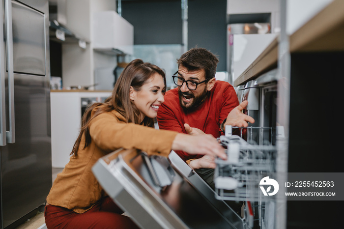 Happy young couple buying dishwasher in store.