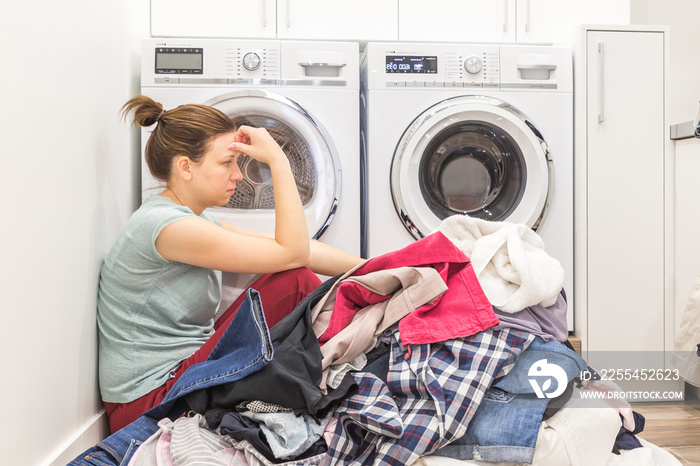 Upset woman in laudry room sitting ona floor with dirty clothes